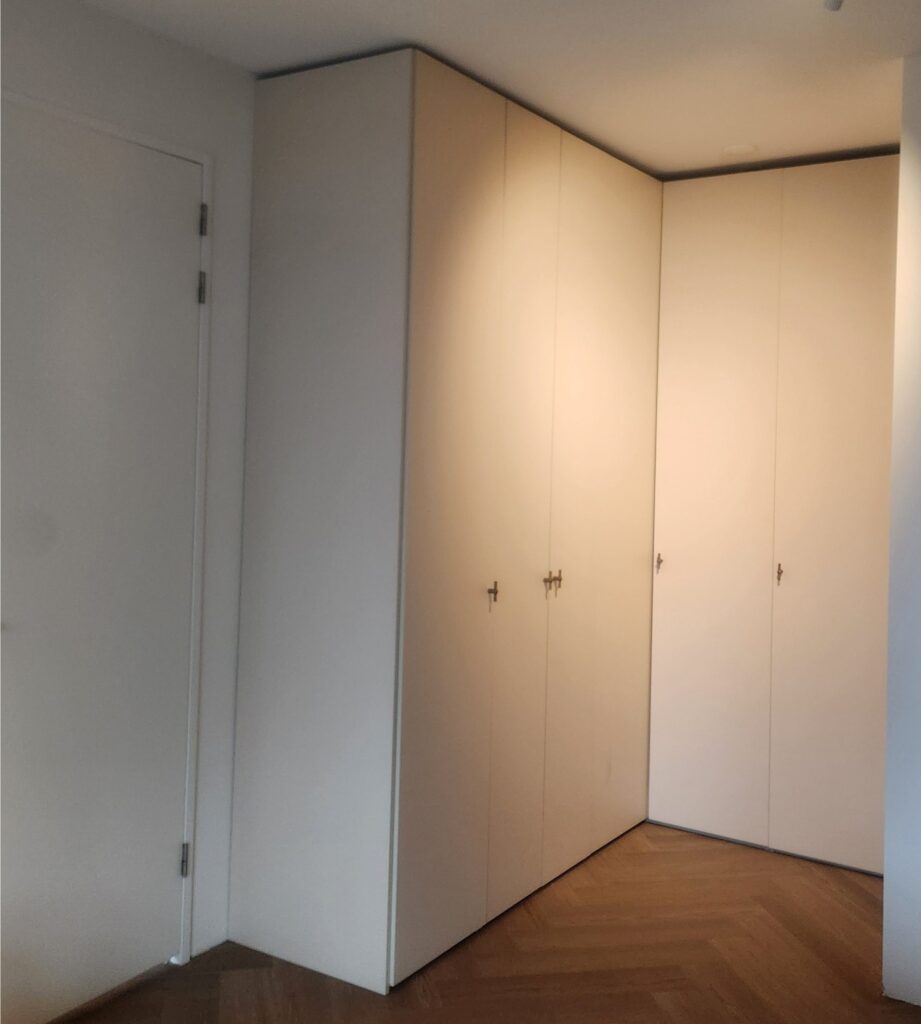Op maat geplaatste IKEA PAX kastopstelling in een slaapkamer, uitgevoerd met strakke witte fronten van vloer tot plafond voor maximale opbergruimte.